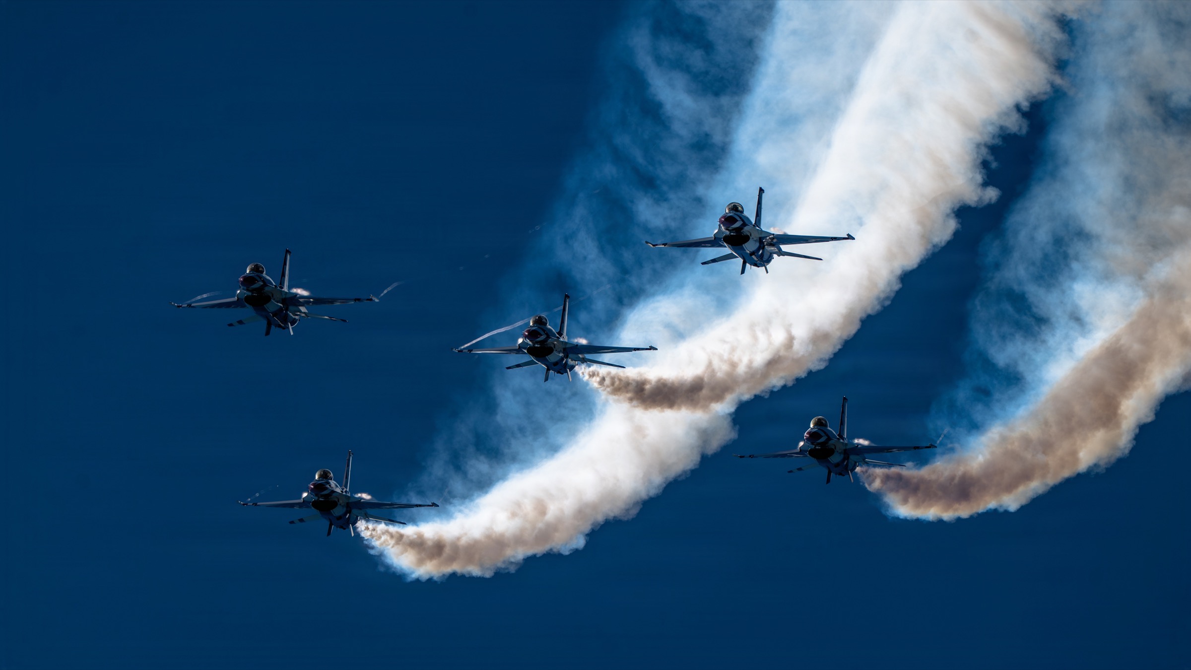 USAF Thunderbirds flying in formation with sweeping smoke trails